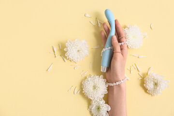 Female hand holding clitoral sex toy on light yellow background