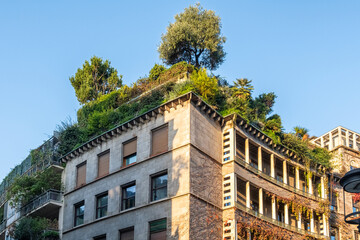 Urban building with lush rooftop garden, featuring trees and greenery cascading over the structure,...