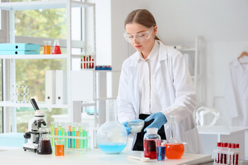 Female chemist with reagents and microscope on table in laboratory
