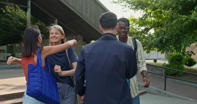 A group of young people hug and say goodbye standing near a glass building. Summer day