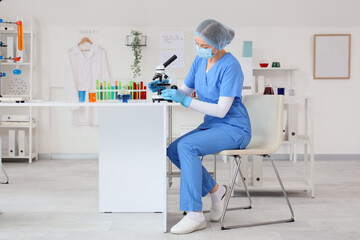 Obraz premium Female chemist with microscope sitting at table in laboratory