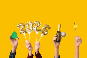 Female hands with figure 2025 made of foil balloons, bottle of champagne, Christmas decorations and...