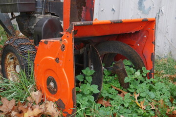 Color photo of an old snowblower with weeds growing inside of it