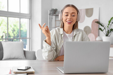Young woman in headphones video chatting with laptop on table at home