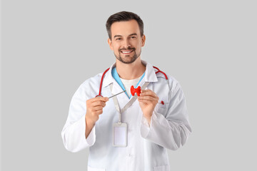 Male endocrinologist with thyroid gland model on grey background