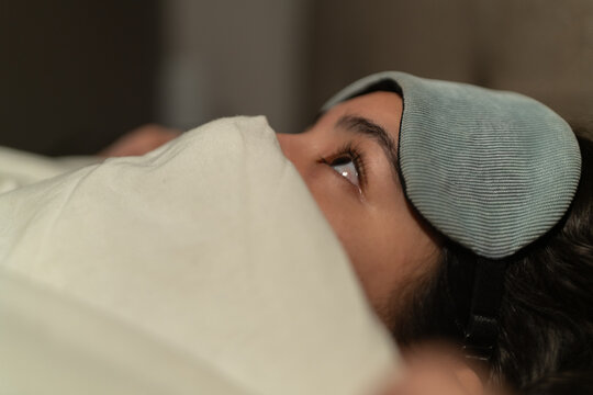 Woman suffering from insomnia lying in bed at night wearing sleeping mask