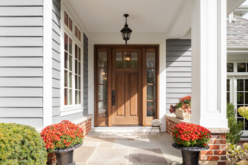 A front door and covered porch detail on a home with grey siding, white trim, red brick, a wooden...