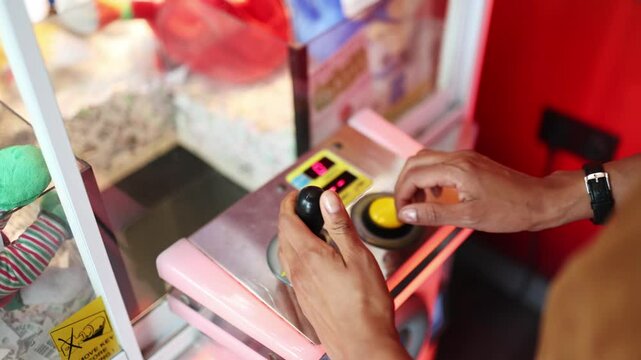 Woman attempts to win a prize at a claw crane game, showcasing skill and luck in a colorful arcade setting.  Woman playing claw crane game trying to grab a prize