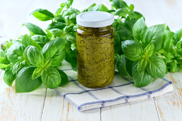 Jar of tasty pesto sauce with basil leaves on a white table.