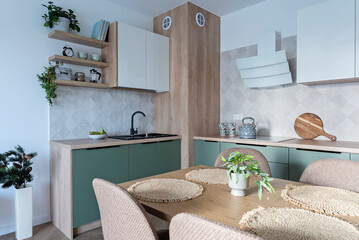 Modern kitchen interior with wooden furniture and counter with kitchen sink. Beige tiles on the wall and table with chairs. Design home with dining room. Real estate.