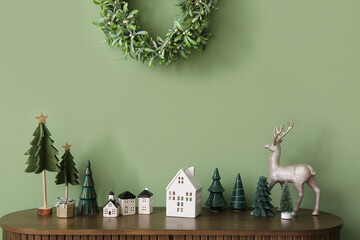 House shaped candle holders with Christmas trees and reindeer on commode near green wall