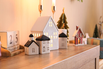 House shaped candle holders and calendar with date of Christmas on commode in room, closeup