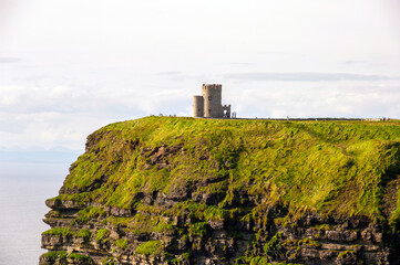 A rocky cliff with a green grassy hillside and a small tower in the distance