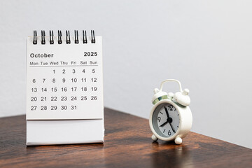 October 2025 calendar and alarm clock on a wooden desk - month page