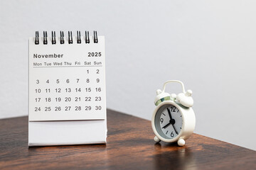 November 2025 calendar and alarm clock on a wooden desk - month page