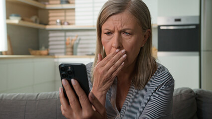 Shocked mature senior Caucasian woman female old lady elderly granny anxious sad look mobile phone...