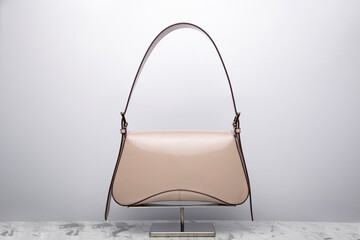 Luxury women's bag on a white background. Beige color, patent leather expensive bag isolated on the marbel in the studio