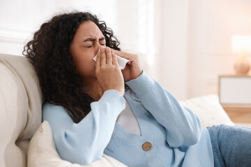 Young woman with tissue blowing runny nose at home