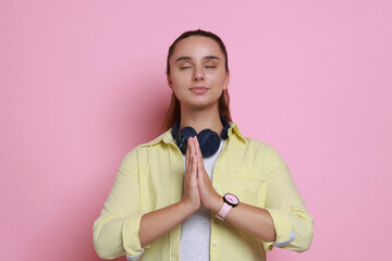 Young student praying for good exam result on pink background