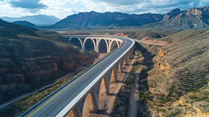 Naklejka premium Majestic highway arch bridge gracefully curving through a rugged, mountainous landscape under a partly cloudy sky. A breathtaking view!