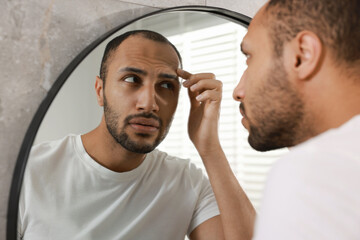 Worried man looking at mirror in bathroom