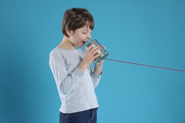 Boy using tin can telephone on blue background
