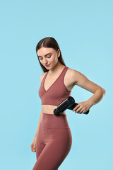 Obraz premium Woman using percussive massager to relieve abdominal muscles on light blue background