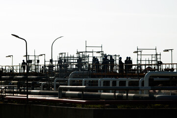 Silhouettes of industrial workers standing on scaffolding amidst pipelines in an industrial facility located in Sines, Portugal.