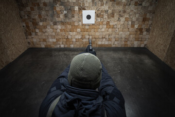 A man in tactical gear practices shooting a pistol with a silencer at a target at a shooting range.