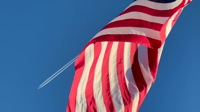 Military aircraft flying past American flag on blue sunny day 
