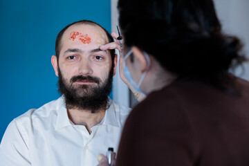 Girlfriend helping man prepare for halloween festivity, dressing him as evil scary zombie. Woman...