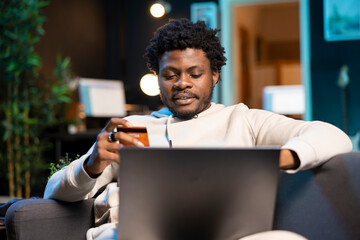 Happy man stoked on doing online shopping, carefully typing credit card information on computer....
