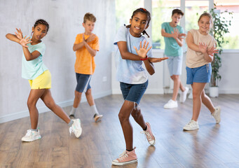 Fototapeta premium Positive juvenile boy engaged in Hip-hop dance together with children's group in training room during workout session