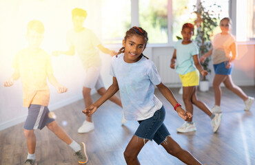 Dynamic little boy training Rock-and-Roll dance poses in dancehall with other attendees of dancing...