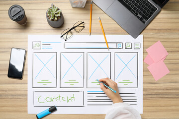 Website designer creating wireframe on paper with pen at wooden table, top view