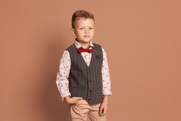 Portrait of little boy with stylish clothes on brown background