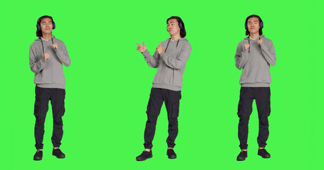 Obraz premium Person listening to music and dancing on camera with audio headset, having fun with songs and funky dance moves. Positive guy feeling optimistic and happy, full body greenscreen backdrop.