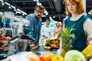 Curious customer looking at another customer's groceries at supermarket checkout