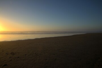 Sun setting over the ocean, with the beach in the foreground and the sky turning a warm shade of orange. 