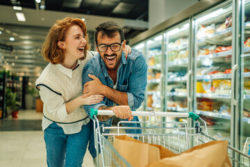 Cheerful couple having fun while shopping for groceries in supermarket