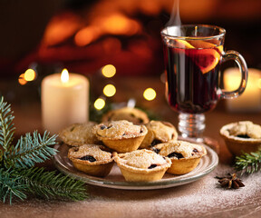 A Christmas atmosphere with mince pies on a plate, a steaming mug of mulled wine with lemon, a fireplace in the background, and a star anise sprig. Perfect for cozy, festive moments with loved ones.