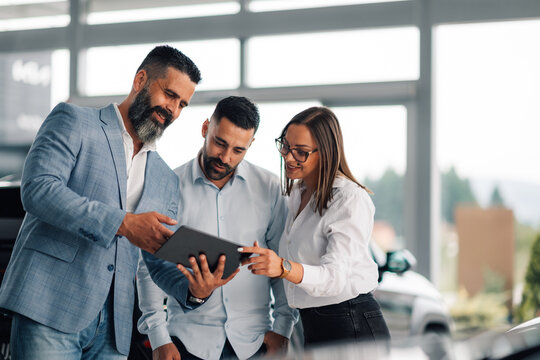 Car dealer showing digital information to interested couple.