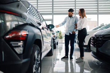 Couple examining the exterior of luxury car in dealership showroom