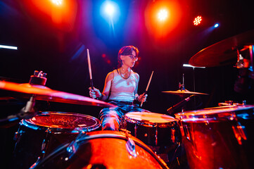 Female drummer performing energetically on stage with colorful lighting