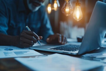 Obraz premium A professional atmosphere, presenting a focused man working at his laptop amidst warm, vintage-style lighting and documents, conveying productivity and creativity.
