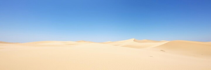 Vast sandy dunes stretch across a barren island desert landscape under a bright blue sky, solitude, desert