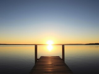 Obraz premium A serene evening scene at the dock with the sun setting in the background, reflecting off the calm water, dock, peaceful