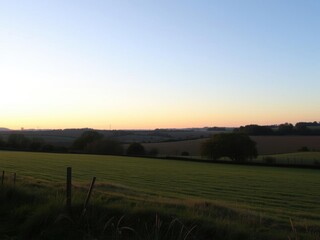 Obraz premium A serene view of the English countryside at dusk, with the soft glow of the setting sun casting a warm hue over the landscape, peaceful, rural