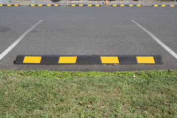 Black and yellow wheel stop parking block in an asphalt parking lot with grass in the foreground