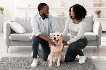 Happy Loving Family. Portrait of beautiful African American spouses patting dog sitting on floor...